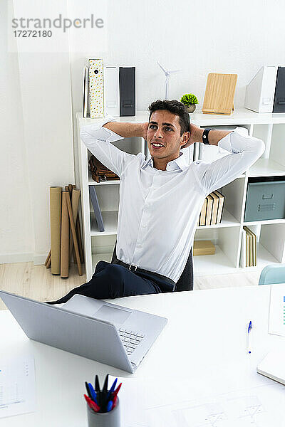 Entspannter Geschäftsmann  der mit den Händen hinter dem Kopf an einem kreativen Arbeitsplatz sitzt