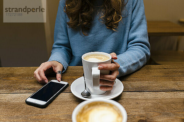 Frau mit Smartphone trinkt Kaffee am Tisch