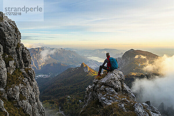 Nachdenklicher Wanderer  der die Aussicht betrachtet  während er bei Sonnenaufgang auf einem Berggipfel in den Bergamasker Alpen  Italien  sitzt