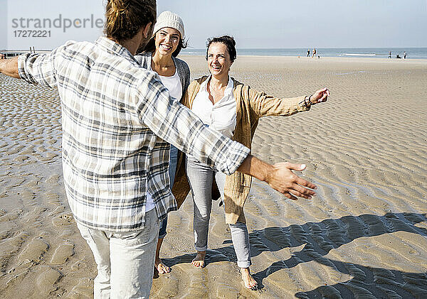 Mann steht mit ausgestreckten Armen am Strand und umarmt Frauen