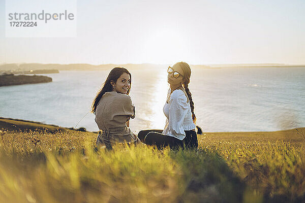 Junge Freundinnen sitzen auf einem Hügel am Mirador de La Providencia  Gijon  Spanien