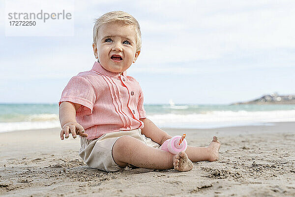 Lächelnder kleiner Junge am Strand sitzend