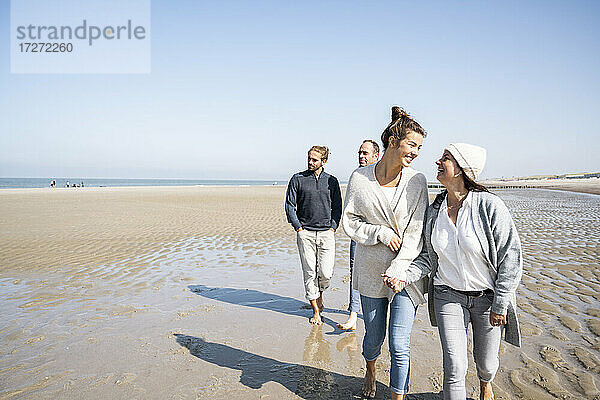 Glückliche Mutter und Tochter spazieren mit Männern im Hintergrund am Strand