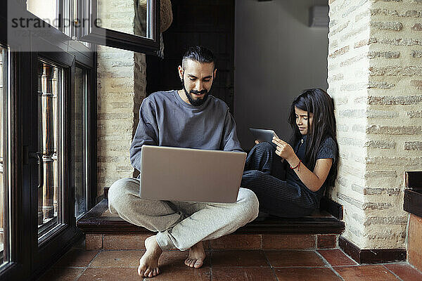 Mädchen benutzt einen digitalen Tisch  während ihr Vater zu Hause am Laptop arbeitet