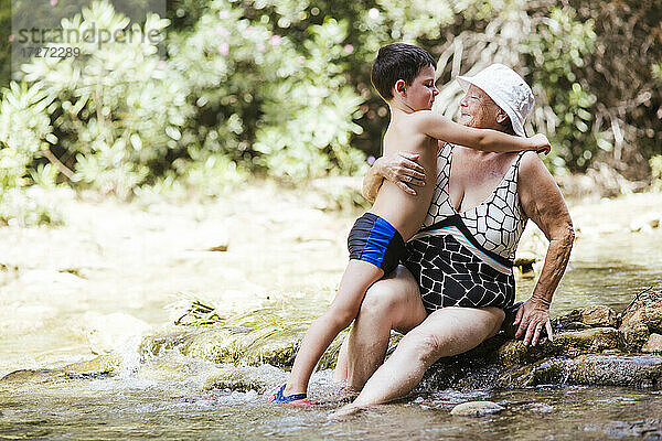 Ältere Frau betrachtet ihren Enkel  der den Arm um sie legt  in einem Fluss im Wald