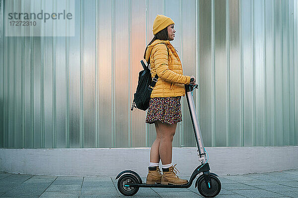 Ältere Frau fährt elektrischen Roller auf dem Fußweg an der Mauer