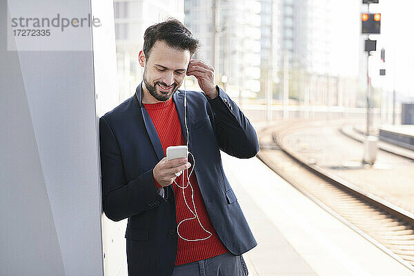 Lächelnder Unternehmer mit In-Ear-Kopfhörern auf dem Bahnsteig