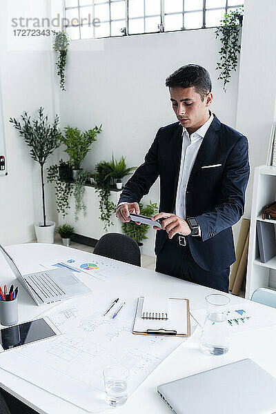 Gut aussehender männlicher Unternehmer  der seinen Schreibtisch im Kreativbüro fotografiert