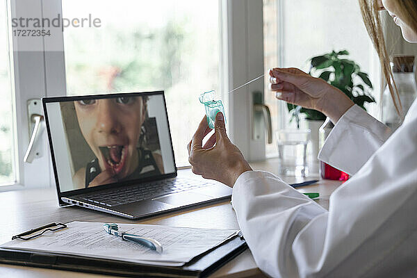 Junge Zahnärztin zeigt einem Patienten Zahnseide per Videoanruf auf dem Laptop zu Hause