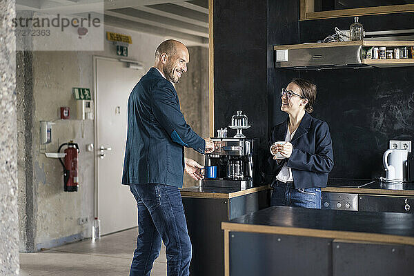 Lächelnde Geschäftsleute  die eine Kaffeepause machen  während sie in der Cafeteria im Büro stehen