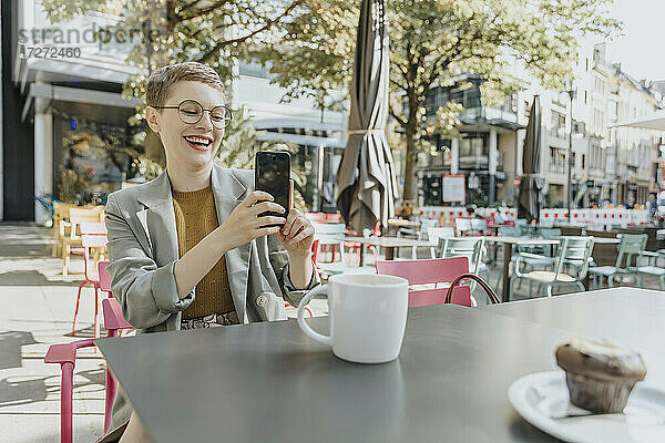 Frau  die ein Selfie mit ihrem Smartphone macht  während sie in einem Café im Freien sitzt