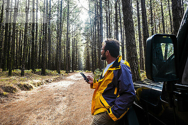 Mann mit Hand in der Tasche  der ein Mobiltelefon benutzt  während er im Wald im Nationalpark El Teide steht  Teneriffa  Spanien