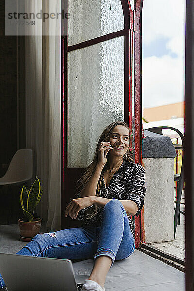 Lächelnde kreative Geschäftsfrau  die mit ihrem Handy telefoniert  während sie an der Tür im Büro sitzt