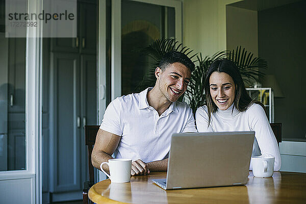 Freund und Freundin trinken Kaffee und benutzen einen Laptop  während sie zu Hause sitzen
