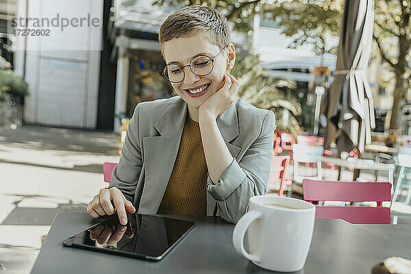 Frau mit digitalem Tablet sitzend mit Hand am Kinn in einem Straßencafé