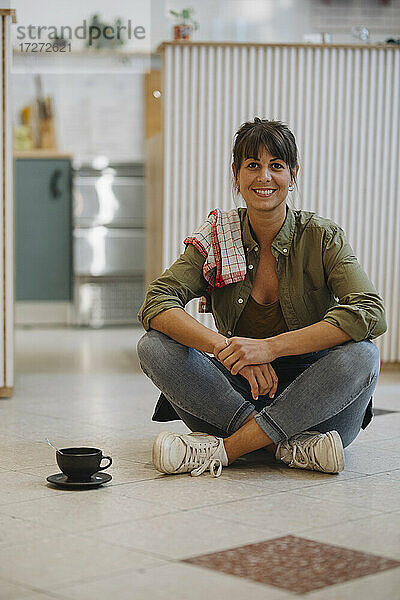 Lächelnde Besitzerin mit gekreuzten Beinen auf dem Boden sitzend in einem Cafe