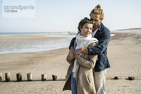 Junges Paar  das sich am Strand umarmt  während es vor einem klaren Himmel steht