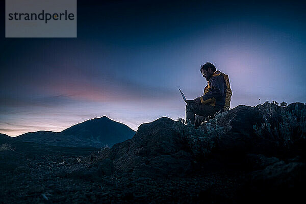 Mann mit Laptop auf einem Felsen sitzend im Nationalpark El Teide  Teneriffa  Spanien