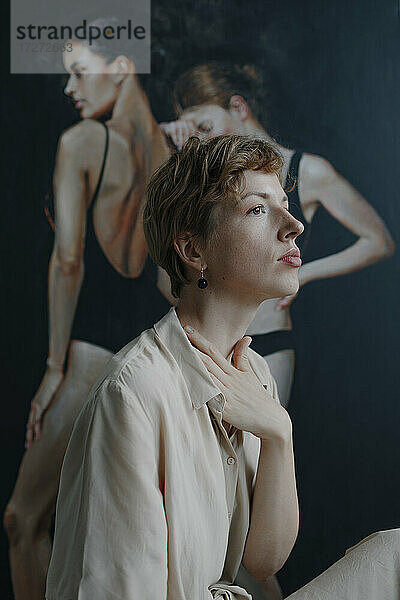 Nachdenkliche erwachsene Künstlerin  die mit der Hand im Nacken wegschaut  während sie beim Malen sitzt