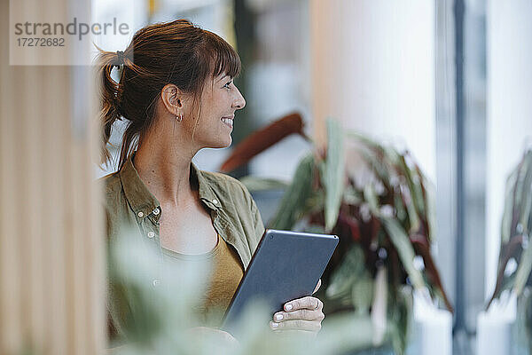 Weibliche Unternehmerin schaut weg  während sie ein digitales Tablet in einem Café hält