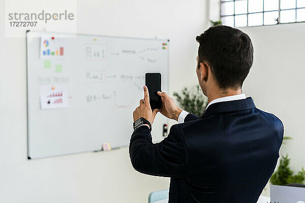 Männlicher Unternehmer  der mit seinem Smartphone im Büro eine Strategie auf einem Whiteboard fotografiert