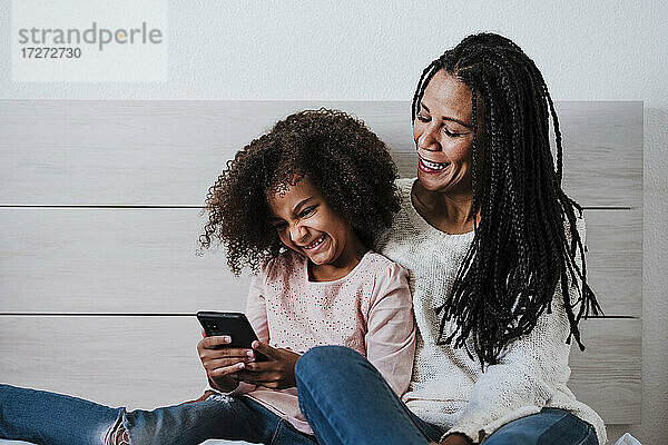 Lächelnd Tochter Textnachrichten auf Smartphone mit Mutter auf Bett im Schlafzimmer zu Hause
