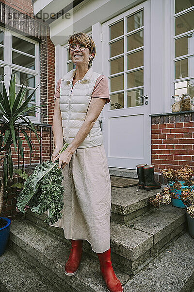 Mittlere erwachsene Frau  die ein Grünkohlblatt hält  während sie im Hinterhof steht