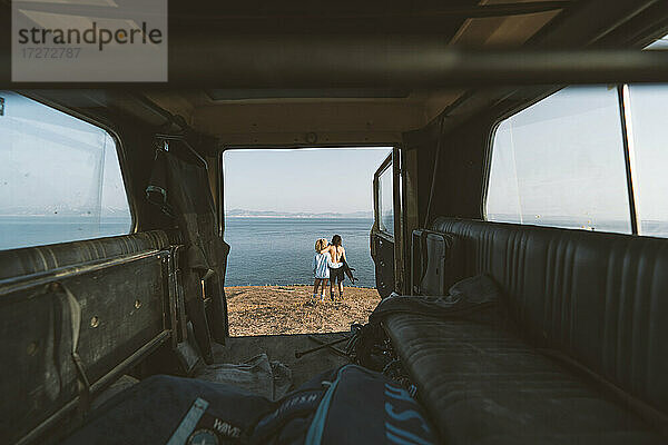 Paar bewundert die Aussicht  während es mit dem Arm am Strand steht