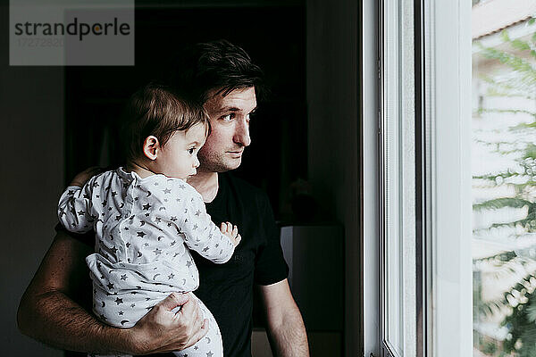 Vater trägt seinen Sohn  während er zu Hause durch das Fenster schaut