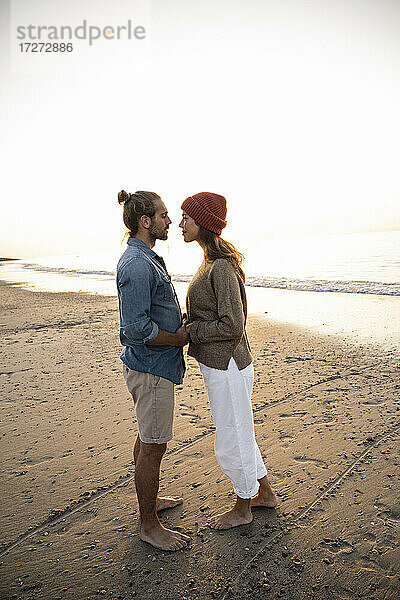 Romantisches junges Paar  das sich bei Sonnenuntergang am Ufer stehend anschaut und die Hände hält