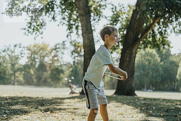 Kleiner Junge wirft Frisbee-Ring  während er in einem öffentlichen Park an einem sonnigen Tag steht