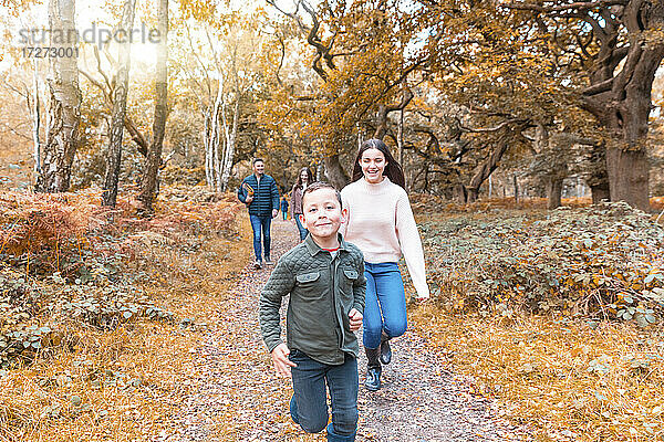 Bruder und Schwester laufen fröhlich  während die Eltern im Herbst im Park von Cannock Chase spazieren gehen