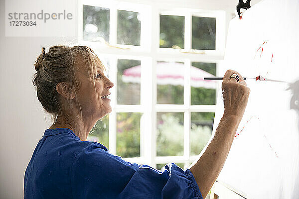 Ältere Frau malt zu Hause ein Bild auf Leinwand