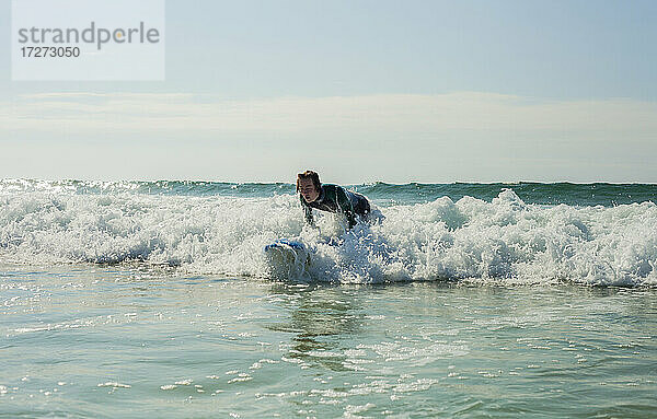 Jugendlicher surft im Meer gegen den Himmel am Strand