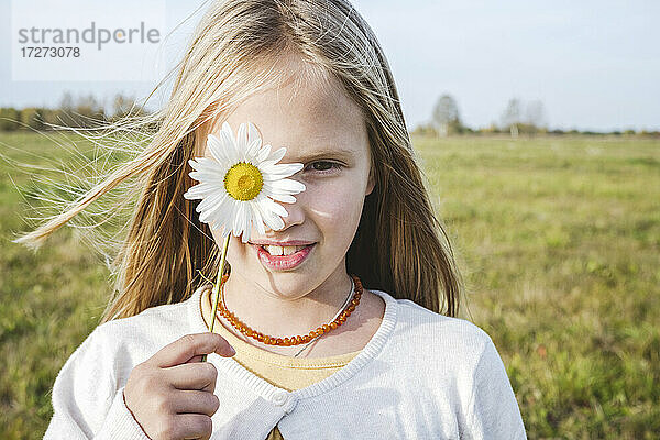 Nettes Mädchen bedeckt Auge mit Kamille Blume auf dem Feld