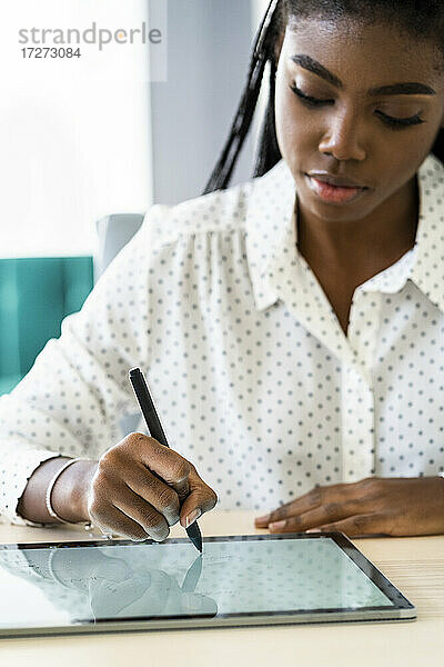 Frau konzentriert sich beim Schreiben auf einem digitalen Tablet im heimischen Wohnzimmer sitzend