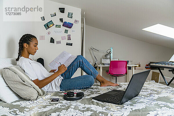 Teenager-Mädchen schreibt in ein Heft  während sie zu Hause auf dem Bett sitzt