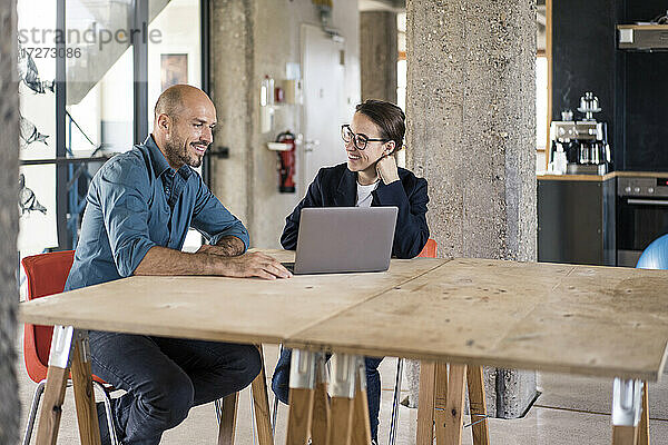Mann und Frau benutzen Laptop  während sie am Tisch im Büro sitzen