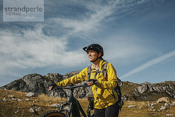 Lächelnde Frau  die mit einem elektrischen Mountainbike gegen einen Berg im Naturpark Somiedo  Spanien  fährt