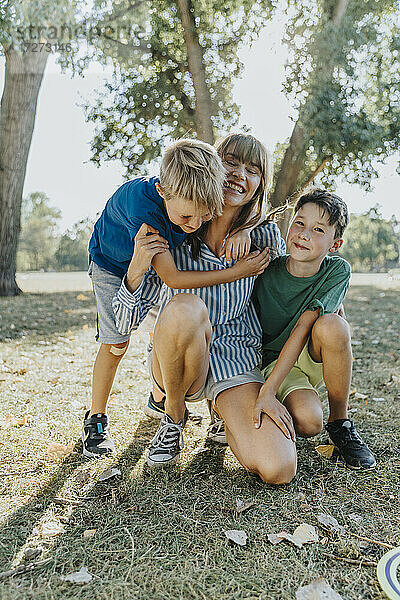 Glückliche Mutter umarmt ihre Söhne in einem öffentlichen Park an einem sonnigen Tag