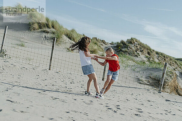 Schwestern spielen auf Sand am Strand während eines sonnigen Tages