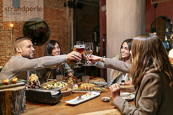 Lächelnde Freunde stoßen auf ein Getränk an  während sie am Tisch im Restaurant sitzen