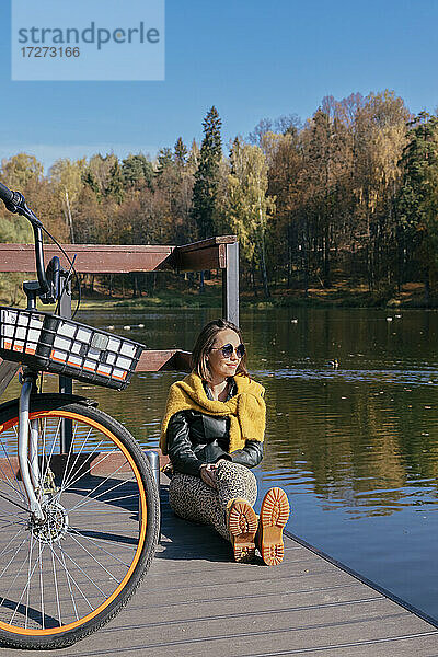 Lächelnde Frau entspannt sich mit dem Fahrrad auf dem Steg über dem See an einem sonnigen Tag