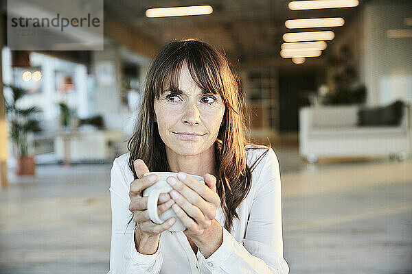 Reife Frau schaut weg  während sie zu Hause Kaffee trinkt