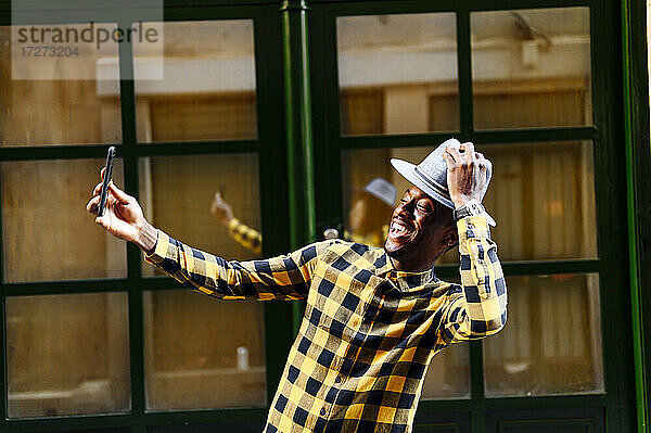 Lächelnder afrikanischer Mann  der ein Selfie mit seinem Mobiltelefon macht  während er in der Stadt steht