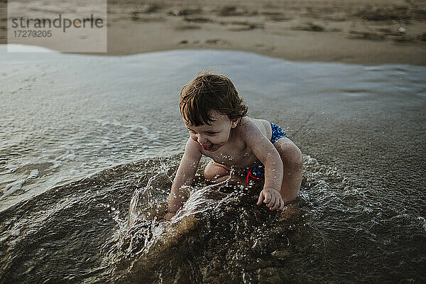 Kleiner Junge spielt im Wasser am Strand bei Sonnenuntergang