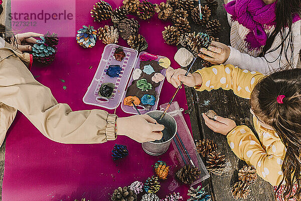 Mädchen dekorieren Tannenzapfen beim Färben am Picknicktisch im Park