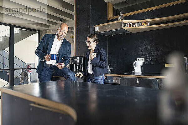 Geschäftsleute  die ein Mobiltelefon benutzen  während sie im Büro Kaffee trinken
