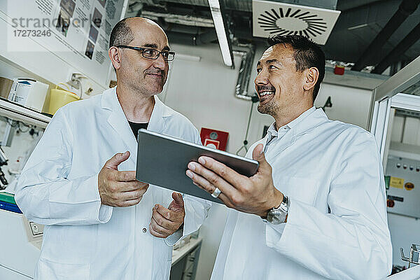 Lächelnde Wissenschaftler  die ein digitales Tablet benutzen  während sie im Labor stehen