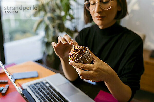 Geschäftsfrau hält Kuchen  während sie zu Hause am Laptop sitzt